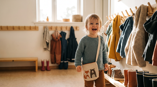 Lachendes Kleinkind mit Kindergartentasche mit Fuchs-Motiv in der Garderobe