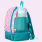 Die Seitenansicht eines blauen Kinderrucksacks zeigt deutlich die elastische Netztasche an der Außenseite, in der eine bunte Trinkflasche sicher verstaut ist. Der Rucksack steht auf einem Holzboden, und das Profil hebt die gepolsterten Schultergurte und den robusten Reißverschluss des Hauptfachs hervor. Die Flasche ist griffbereit platziert, was die Funktionalität für Ausflüge unterstreicht.