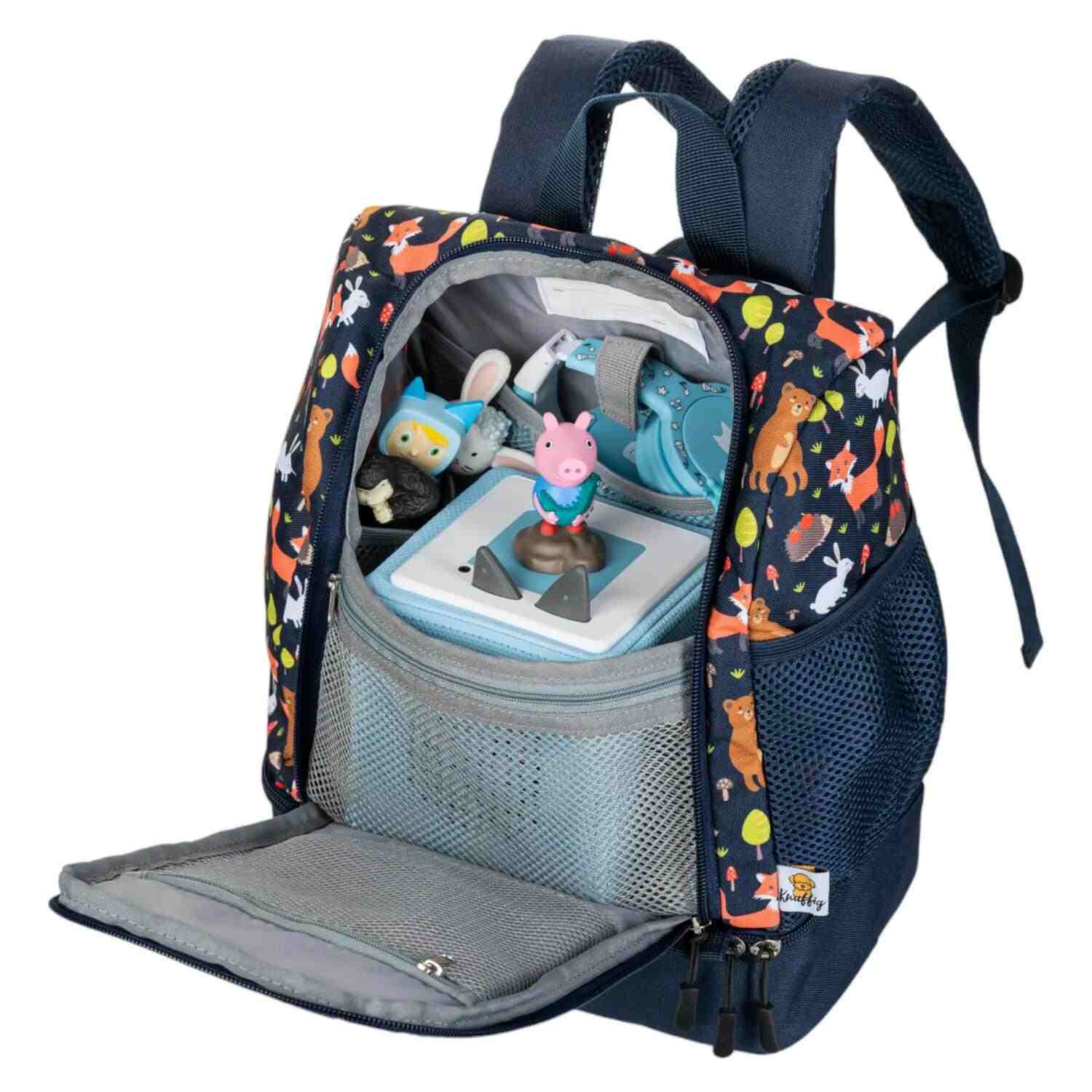 Seitenansicht des prall gefüllten, blauen Kinderrucksacks mit dem Fuchs-Motiv. Die elastische Netztasche an der Seite ist mit einer Trinkflasche und mehreren Tonie-Figuren bestückt. Das stabile, ergonomische Design wird durch die dicke Polsterung der Schultergurte und die gefüllten Fächer sichtbar, was die Kapazität für einen Tag voller Entdeckungen unterstreicht.