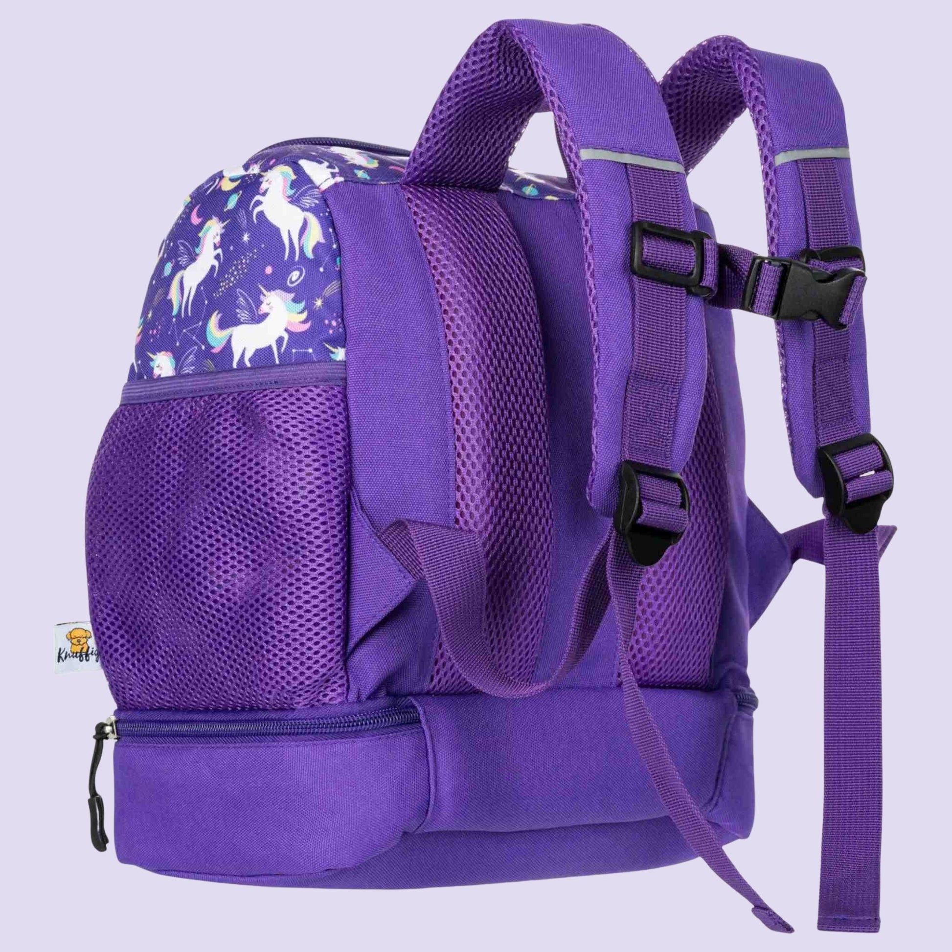 Eine detaillierte Nahaufnahme der Rückseite des lila Einhorn-Kinderrucksacks. Das Bild stellt die ergonomische und dicke Mesh-Polsterung in den Fokus, die durch ihre Wabenstruktur für optimale Luftzirkulation am Kinderrücken sorgt. Gut sichtbar sind die breiten, gepolsterten Schultergurte, der verstellbare Brustgurt und der Tragegriff. Der lila Stoff ist mit kleinen, glitzernden Sternen und Einhörnern verziert. Der Rucksack steht auf einem hellen Holztisch, im Hintergrund ist ein unscharf angedeutetes Kinde