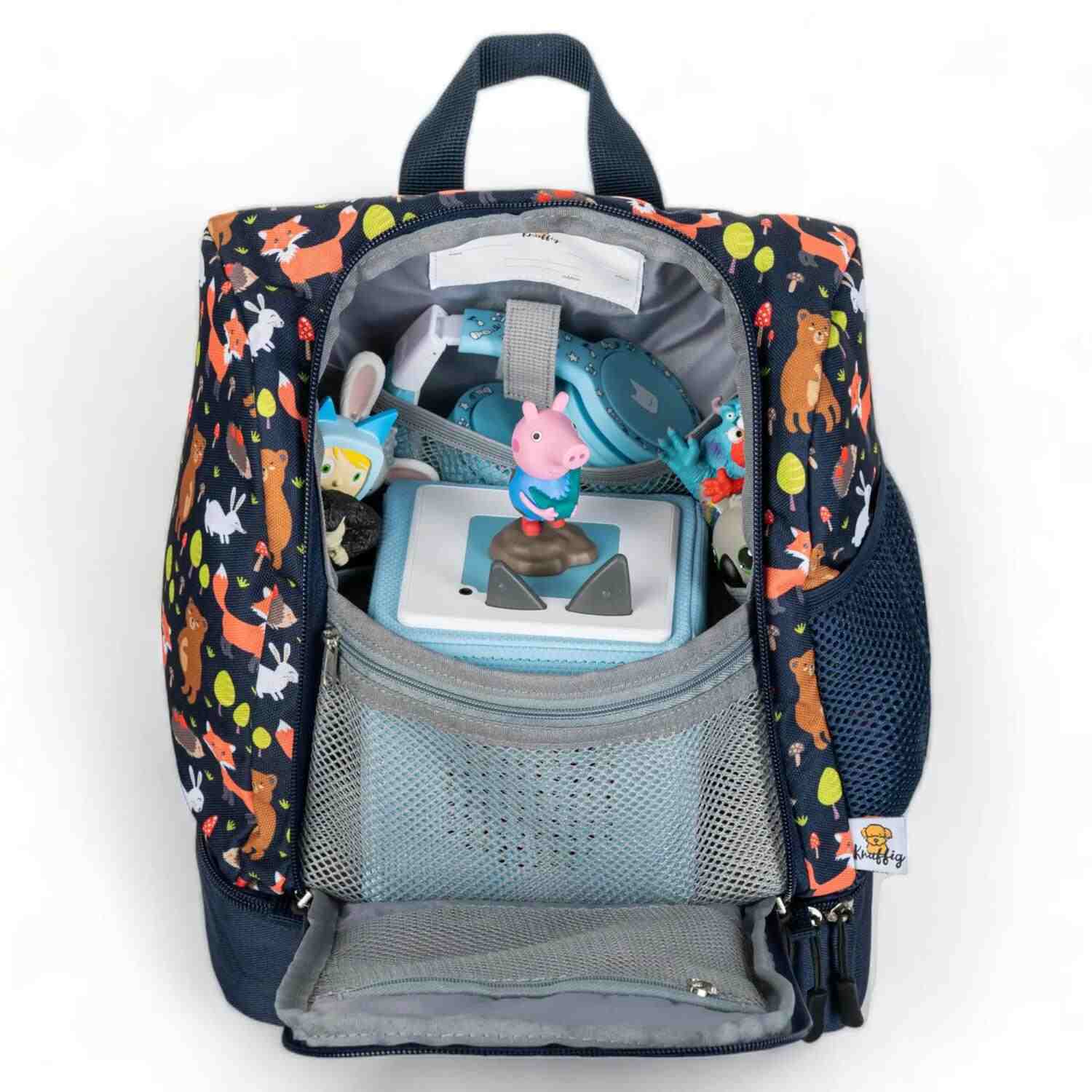 Ein Blick in den voll bepackten blauen Kinderrucksack: Im geräumigen Hauptfach ist eine Toniebox sicher verstaut, während das seitliche Netzfach mit mehreren Tonie-Figuren gefüllt ist. Das Bild zeigt das großzügige Platzangebot, das ideal auf das gesamte Audio-System für Kinder abgestimmt ist.