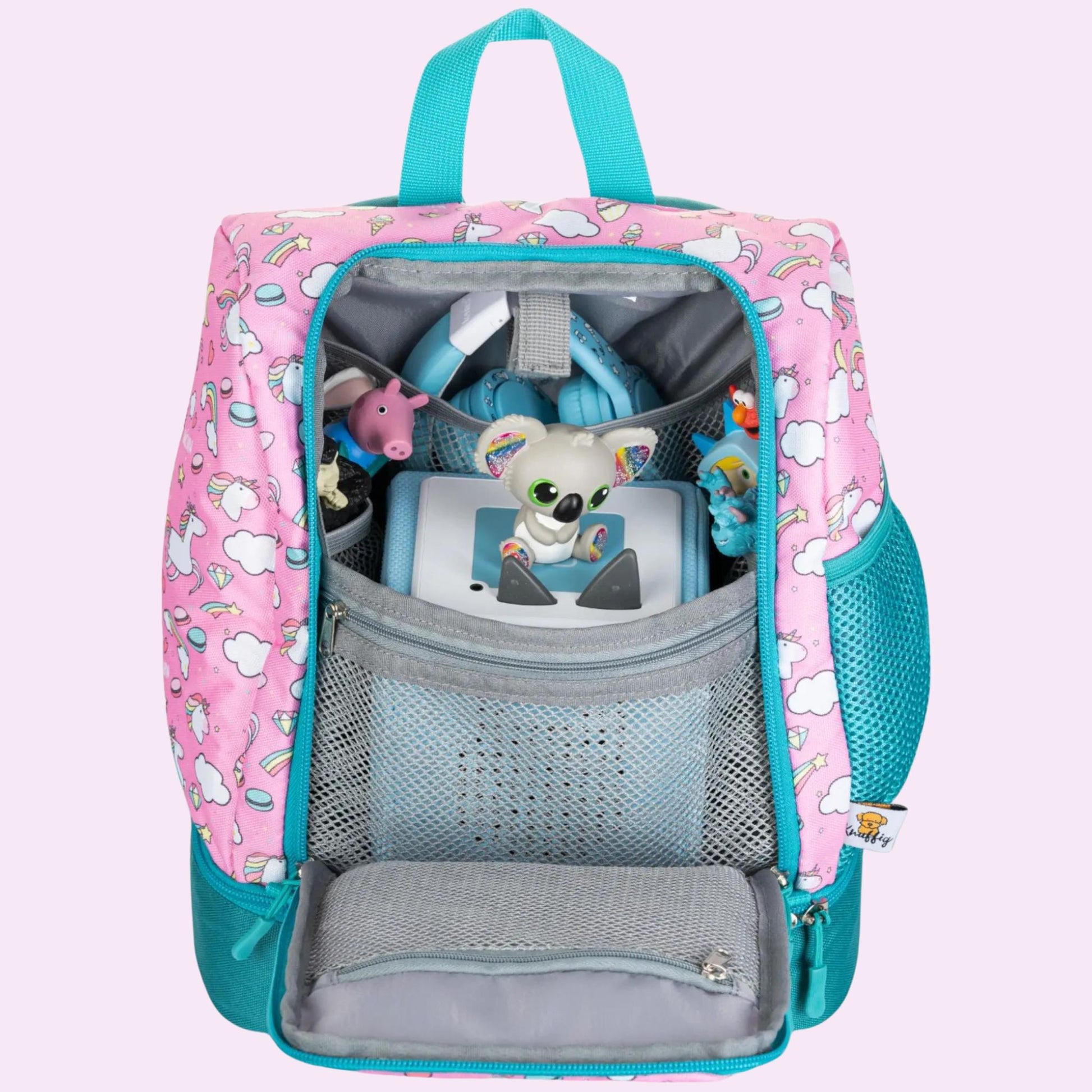 Ein Blick von oben in das weit geöffnete Hauptfach des rosa Einhorn-Rucksacks. Im Inneren ist eine Toniebox perfekt platziert, während mehrere Tonie-Figuren in den dafür vorgesehenen elastischen Schlaufen sicher fixiert sind. Daneben liegt ein Paar farblich abgestimmte Kinderkopfhörer. Die durchdachte Aufteilung zeigt, wie das gesamte Audio-Equipment für unterwegs ordentlich, geschützt und griffbereit verstaut werden kann.