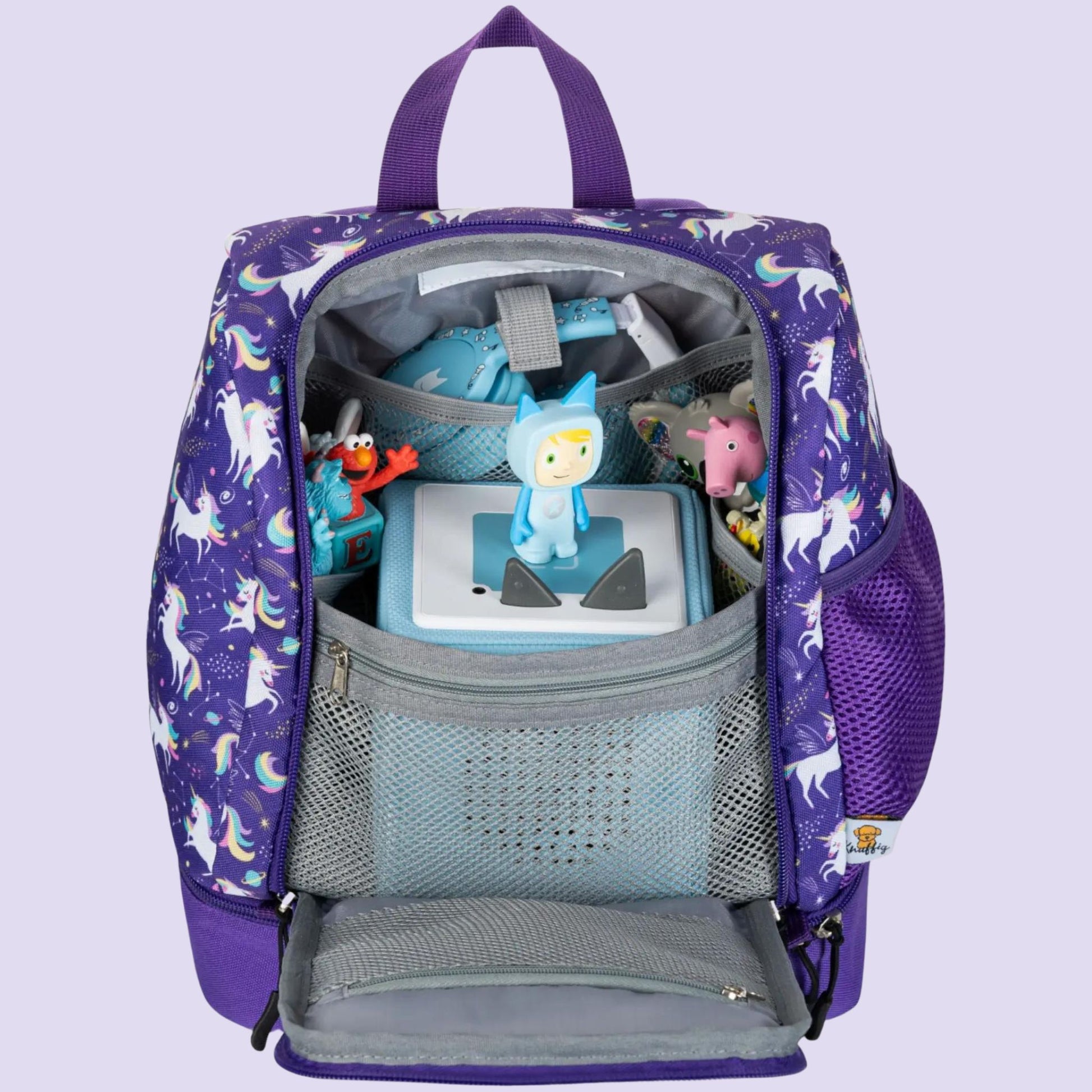 Ein Blick in das weit geöffnete, geräumige Hauptfach des lila Einhorn-Rucksacks. Das Innenleben ist perfekt für Audio-Fans organisiert: Eine Toniebox ist sicher verstaut, während Kopfhörer in einem separaten Fach Platz finden. Mehrere kleine Netztaschen und elastische Halterungen halten die Tonie-Figuren fest an ihrem Platz. Die Aufteilung zeigt, wie das komplette Audio-Equipment stoßfest und übersichtlich für Reisen oder den Kindergartenbesuch untergebracht wird.